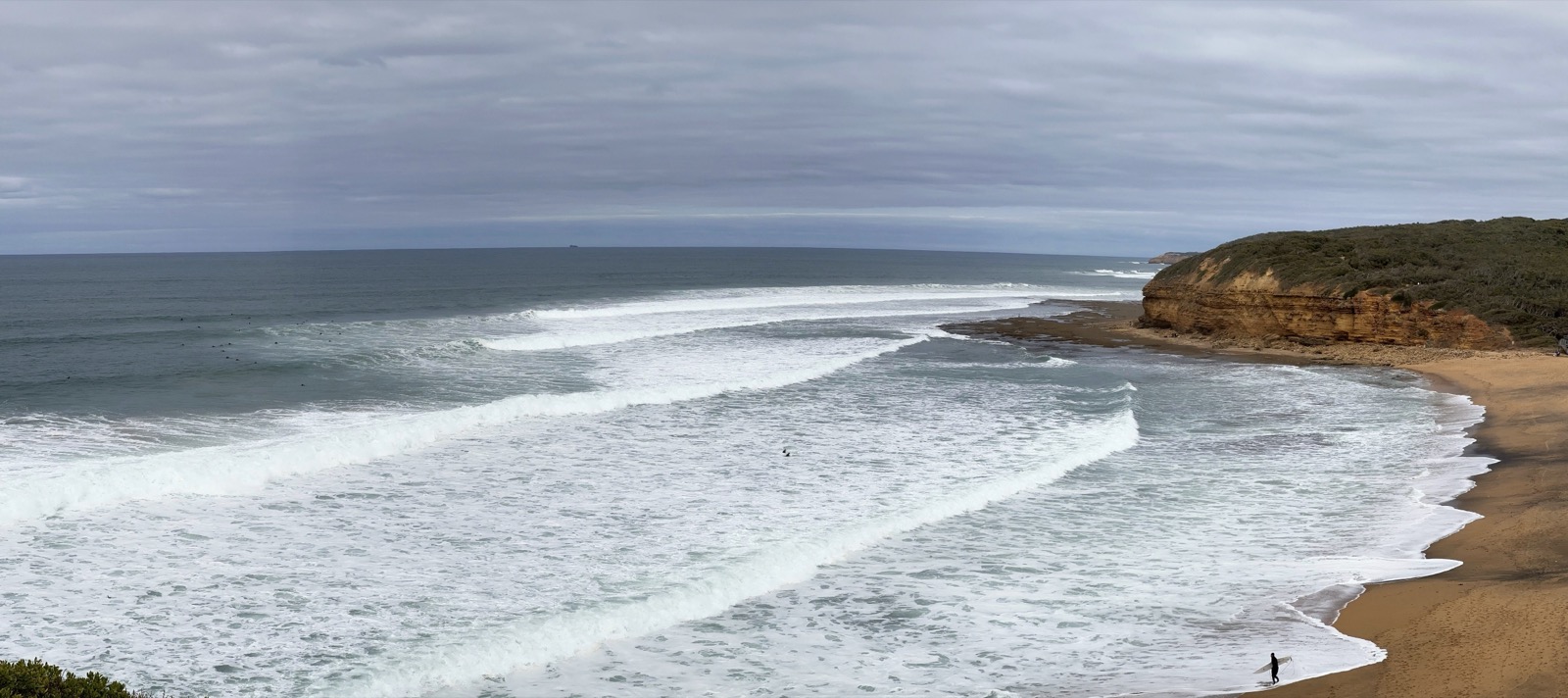 Majestic waves crash along the rugged cliffs of Great Ocean Road, Australia, under a cloudy sky.